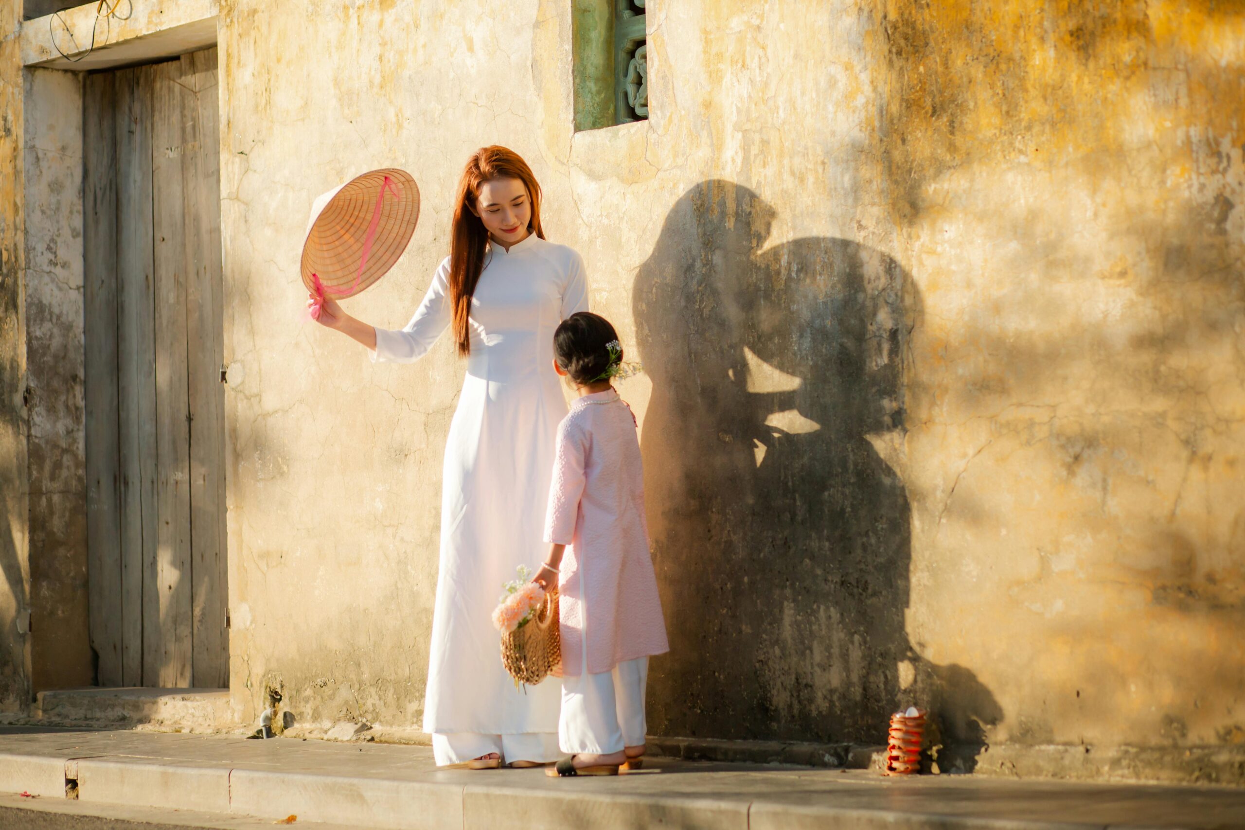 A woman and child in traditional Ao Dai dresses on a sunny day in Hội An, Vietnam.
