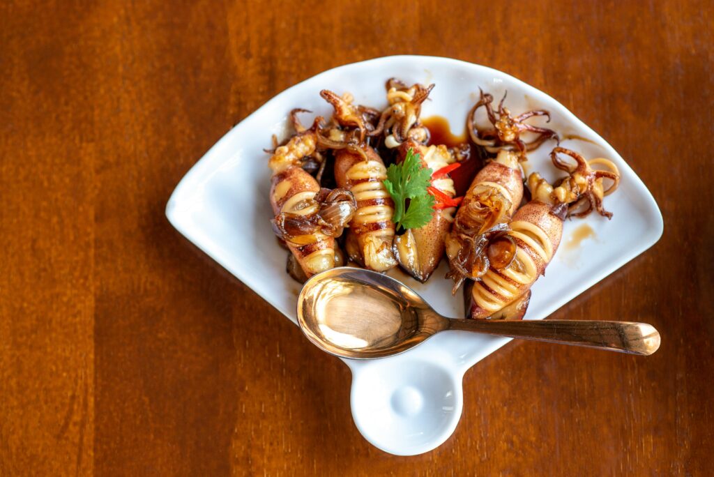 Appetizing grilled squid served with garnishes on a stylish plate with a spoon.